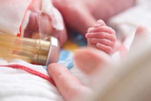 a newborn in an incubator holding a parent’s finger